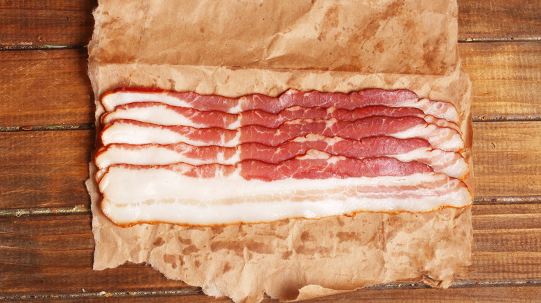 Raw bacon slices on brown parchment paper on a wooden counter