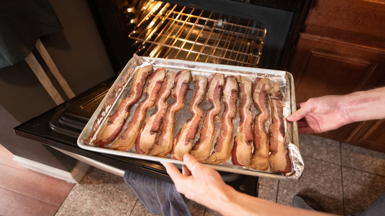 A person places a tray of bacon into an oven