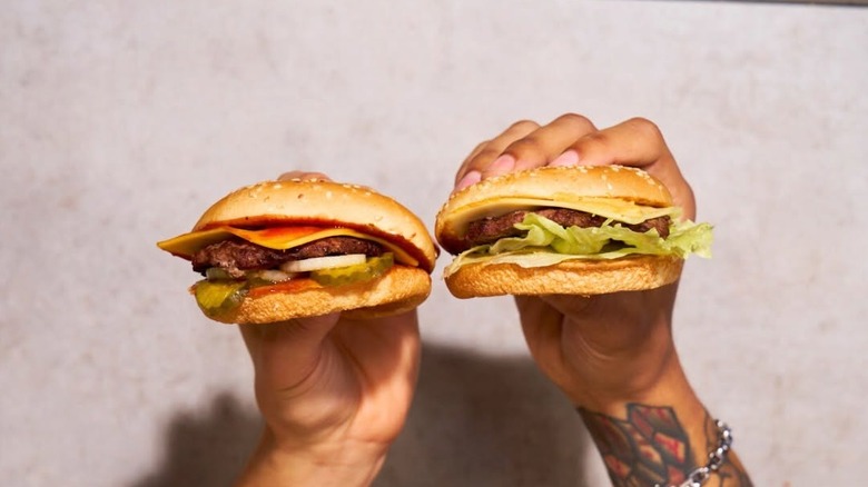 Two hands hold Carl's Jr cheeseburgers.