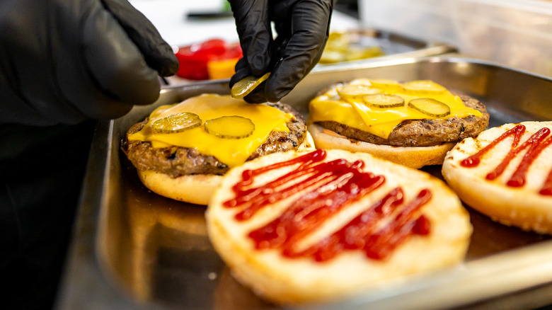 Gloved hands prepare fast food cheeseburgers.