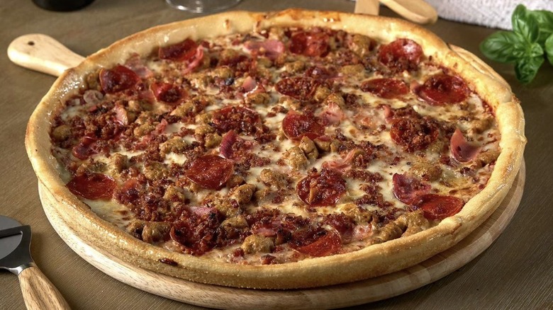 Member's Mark four meat pizza served on a wooden peel near basil and a pizza cutter