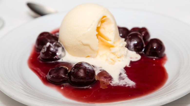 White bowl of cherries jubilee with a scoop of vanilla ice cream