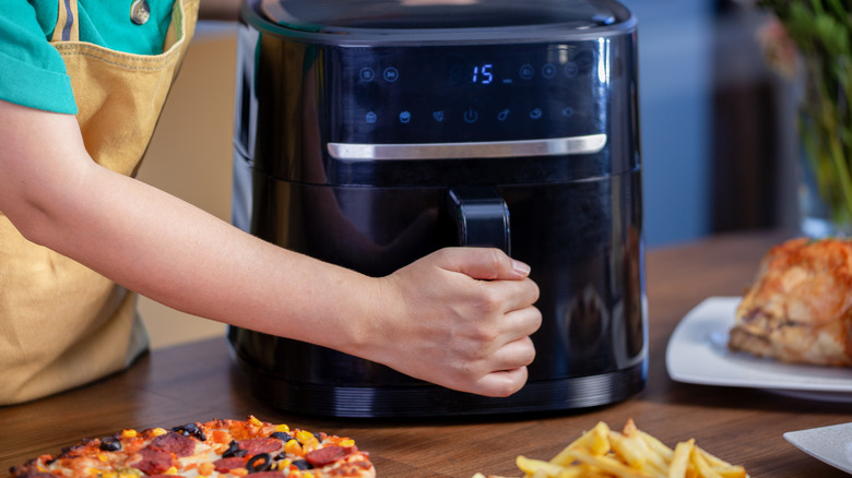 Home cook opening air fryer with various foods around