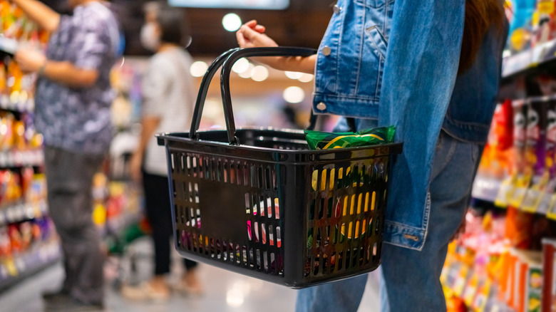 A woman walking down an aisle in the grocery store with a shopping basket