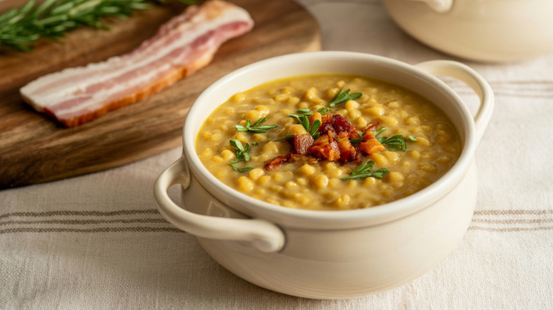 Split pea soup in a bowl, topped with bacon and fresh rosemary.