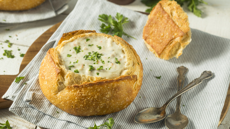 A breadbowl of New England clam chowder, topped with some fresh parsley.