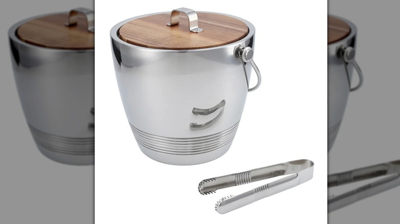 A stainless steel ice bucket with a wooden lid sits next to a small stainless steel pair of tongs