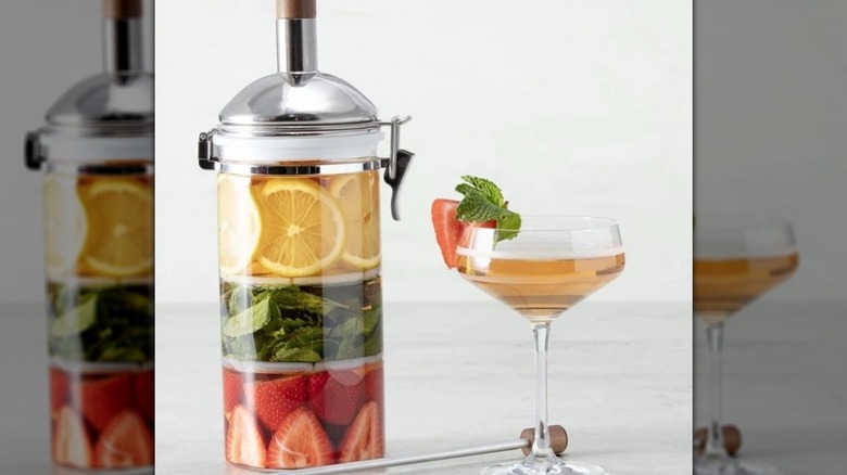 A multi-chambered infusion jar is filled with lemons, mint leaves, and strawberries