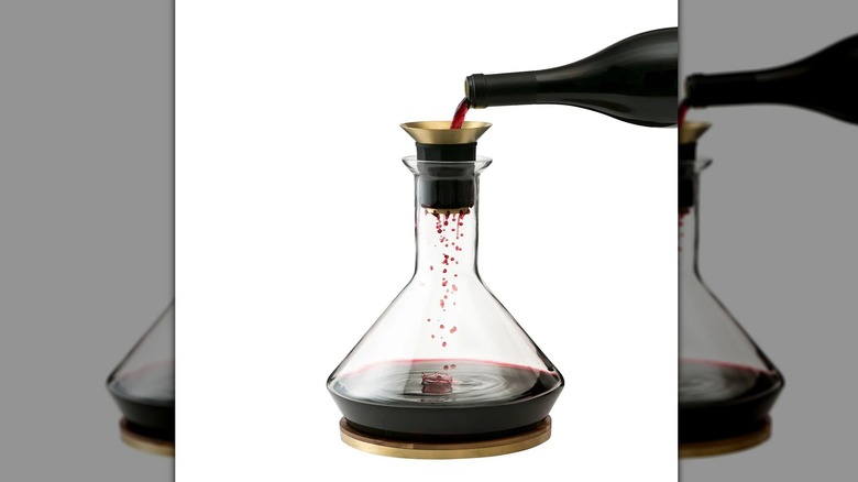 A glass wine decanter with a gold and black filter has wine poured into it