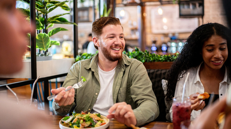 Man dressed casually eating a salad at a restaurant while dining with friends