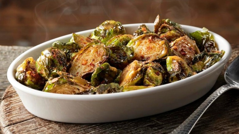 LongHorn Steakhouse crispy Brussels sprouts in a white oval ramekin on top of a wooden cutting board