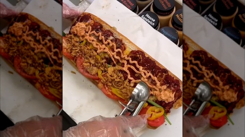 Subway Canada's Tandoori Twist being assembled on a white sheet of paper while a gloved hand is scooping pork into it