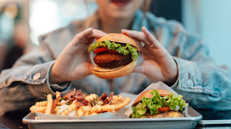 Woman holding mushroom burger over a silver tray of loaded fries and a hamburger