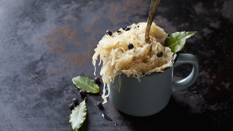 Sauerkraut in a cup with a fork, whole black pepper corns and bay leaves