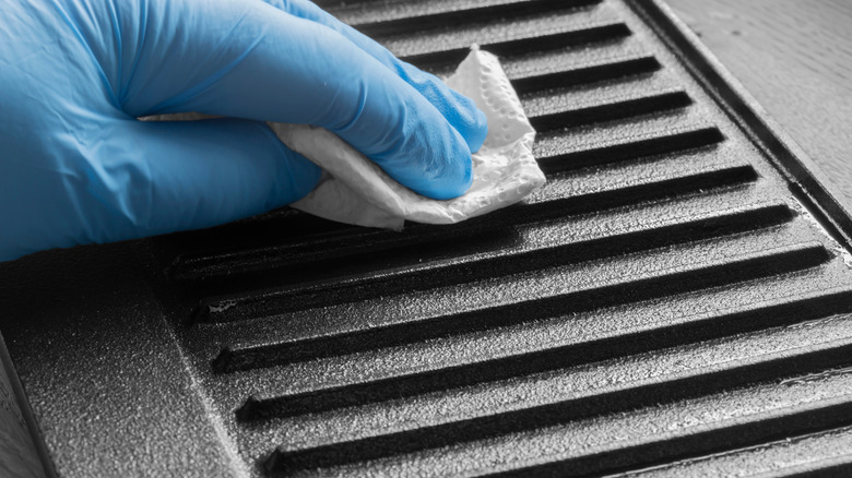 Close up of a blue gloved hand wiping a cast-iron grill pan with oil