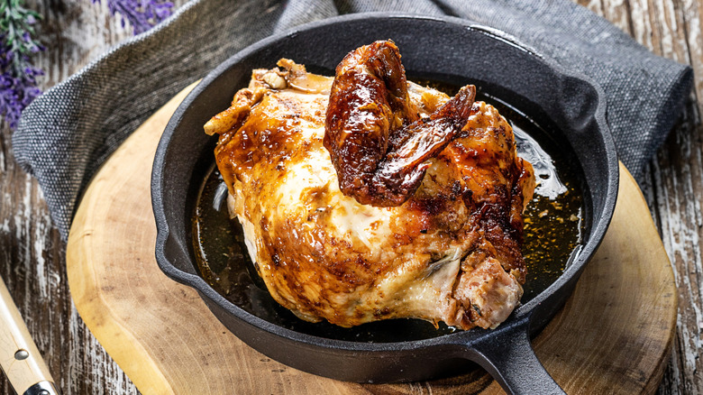 A half chicken lies in a cast-iron skillet on a round wooden cutting board
