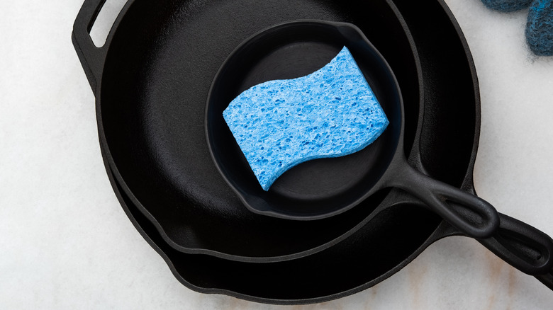 A stack of cast-iron skillets with a blue sponge in the center of the top skillet