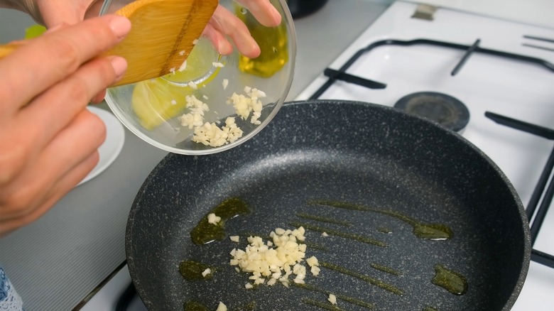 Hands adding chopped garlic to frying pan with oil