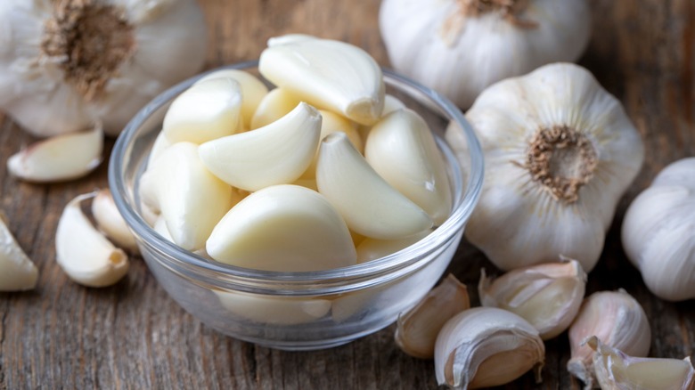 Small bowl of freshly peeled garlic cloves with heads of garlic all around