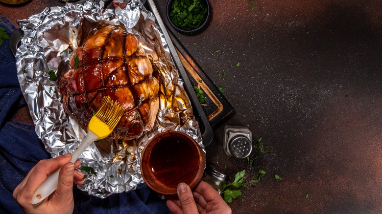 Hands brushing lgaze on a baked ham