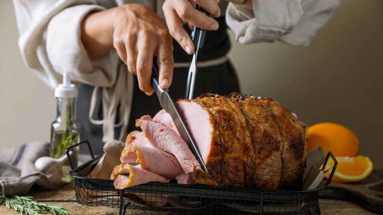 Hands carving a baked ham with a large knife