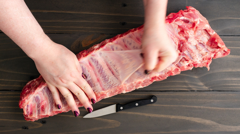 Hands peeling the silverskin from a rack of ribs