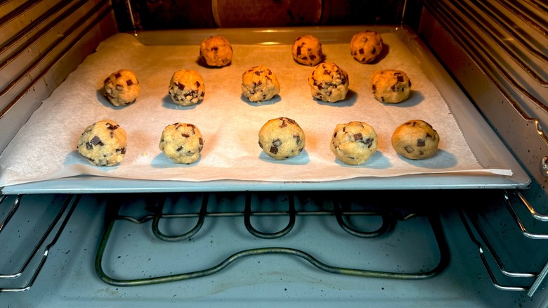 Cookie dough balls on parchment paper-lined baking tray in oven