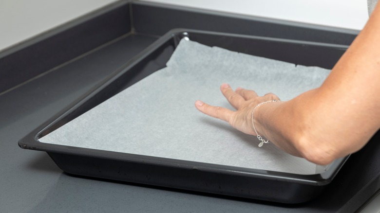 Hand placing parchment paper on baking tray