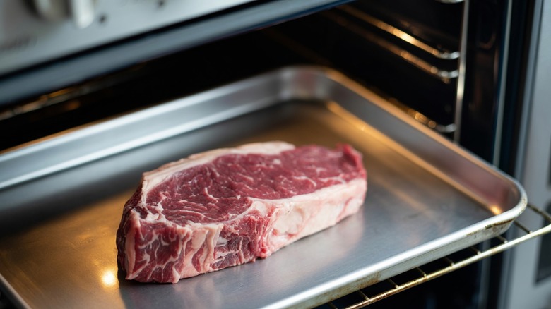 A raw steak sitting on a sheet pan in the oven