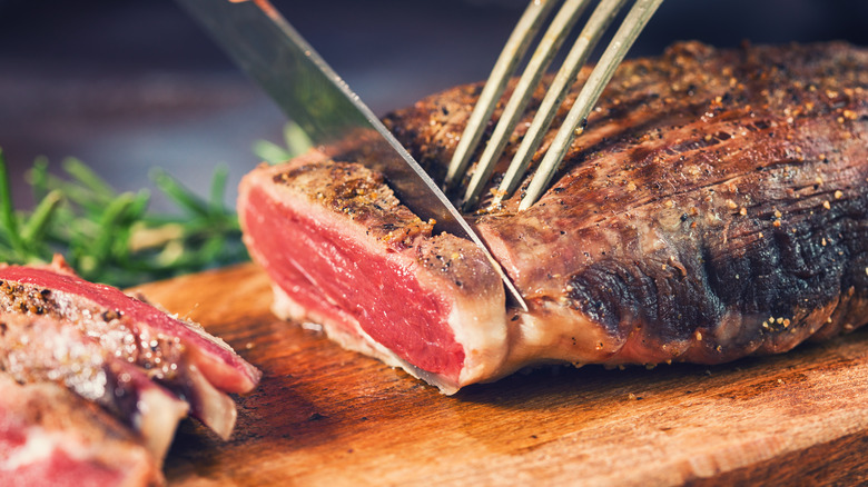 A steak being sliced on a wooden cutting board