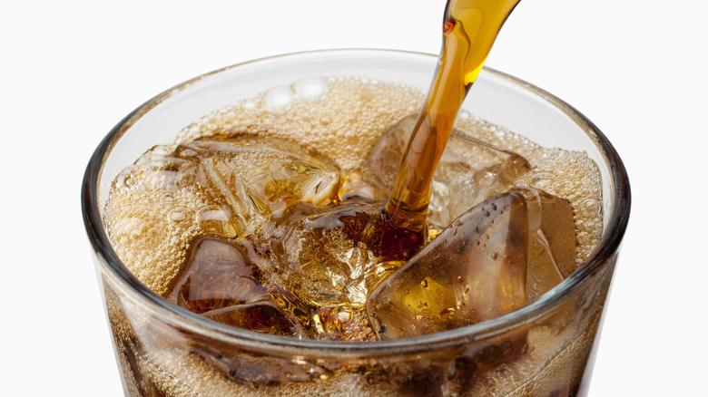 Brown soda pouring into glass with ice