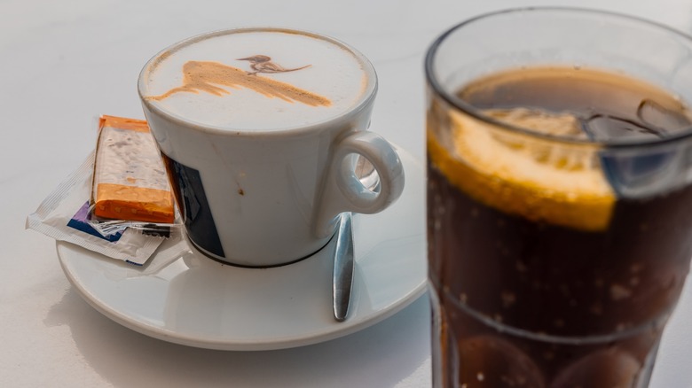 Latte in mug next to glass of soda