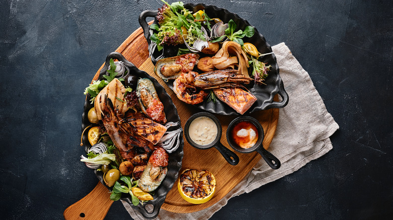 Overhead shot of two seafood platters on a wooden serving board against a grey background