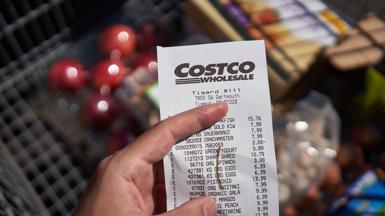 Costco receipt displaying prices held above a shopping cart