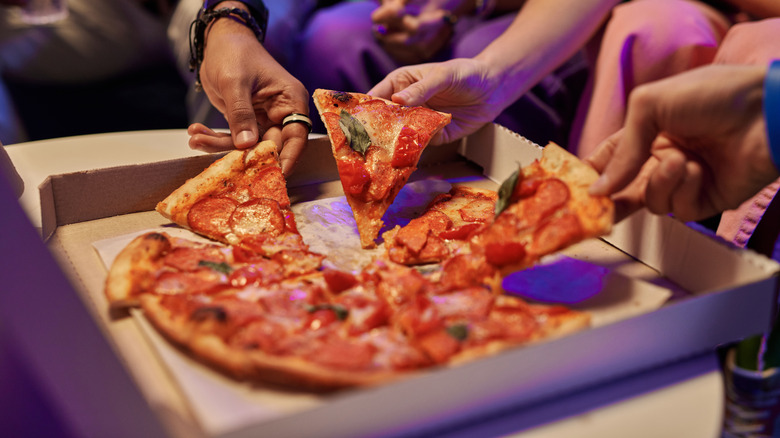 People sharing a pizza from a box.