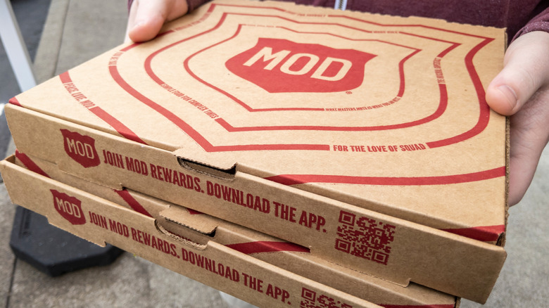 Hands carry MOD Pizza boxes.