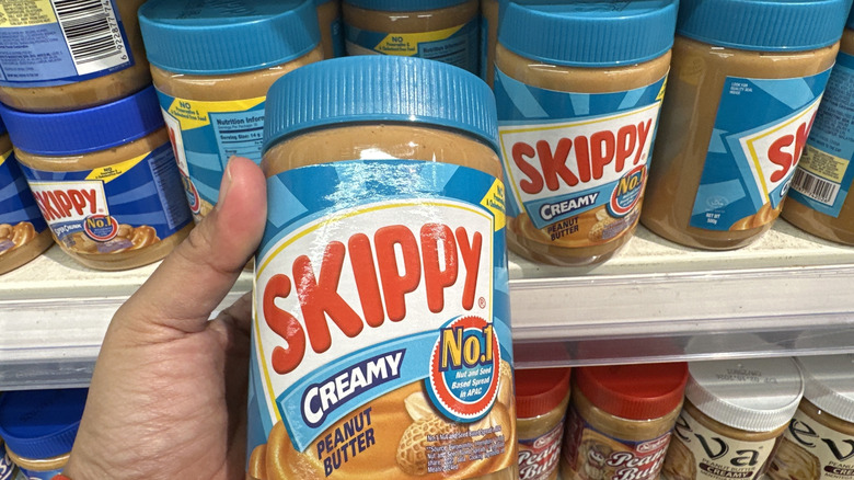 Shopper holds a jar of Skippy peanut butter in a store aisle