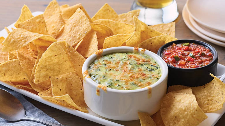 Tortilla chips sitting on a plate with a bowl of Spinach and Artichoke Dip and salsa from Applebee's.