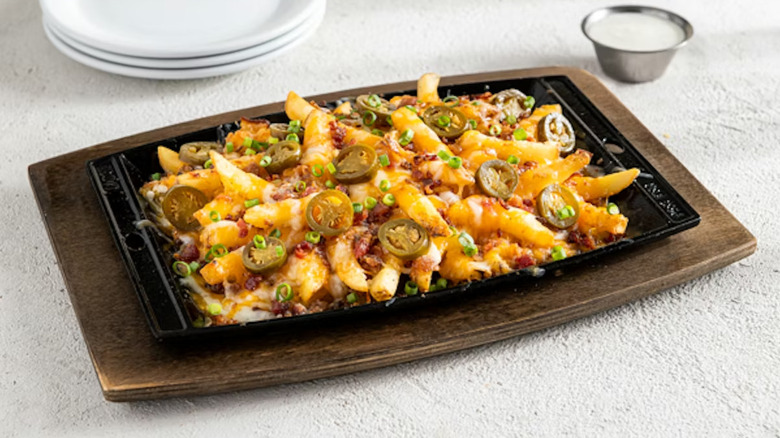 Plate of Chili's Texas Cheese Fries topped with jalapeno slices, cheese, bacon bits, and sliced green onion.