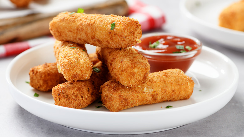 A plate of crispy mozzarella sticks next to a side of marinara sauce in a small dipping bowl.