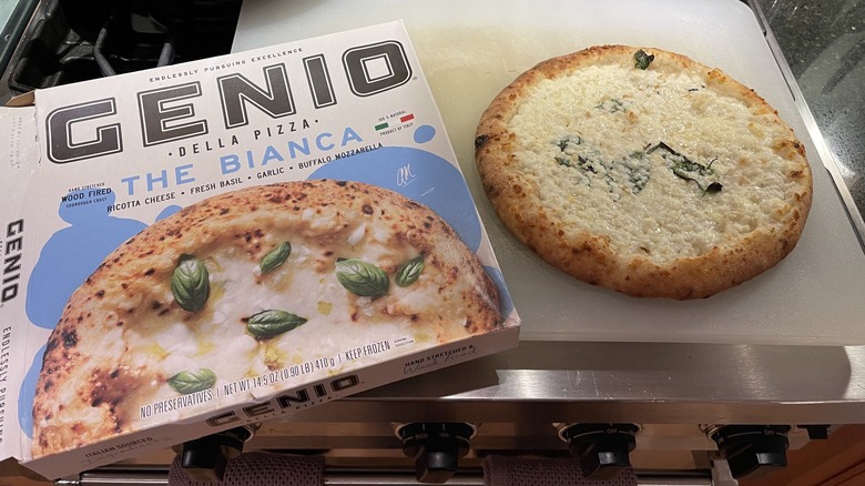 A Genio Della frozen pizza sits on a plastic cutting board