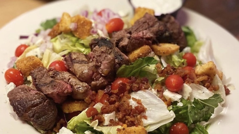 Steak salad with bacon bits, tomatoes, and dressing on the side from Texas Roadhouse