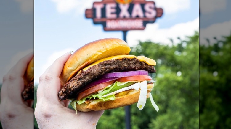 Cheeseburger held aloft in front of an elevated Texas Roadhouse sign