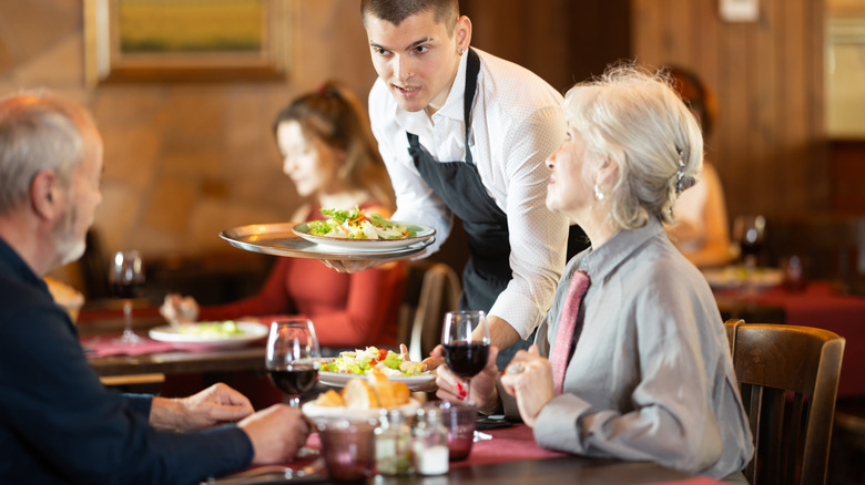 waiter drops off salads to a two-person table with red wine