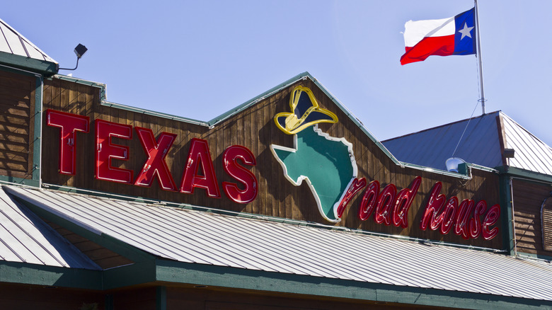 The Texas Roadhouse logo in red lettering with a green Texas in the middle on a wooden building.
