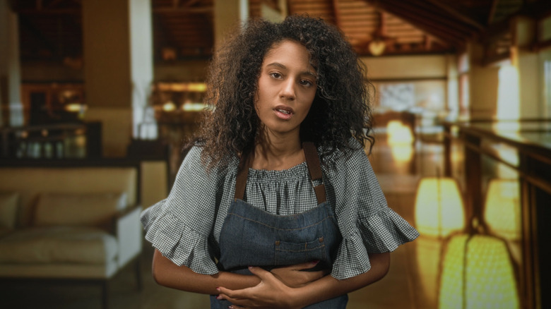 a woman wearing an apron in a restaurant holding her stomach