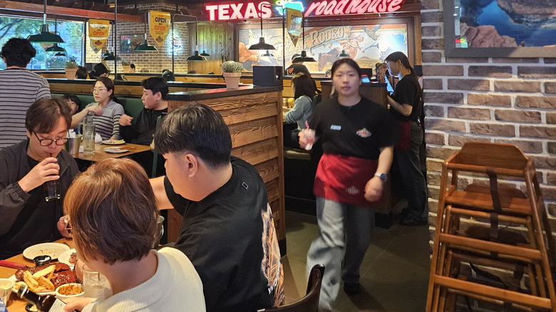 A server carrying a drink with a red apron, black t-shirt, and plain denim jeans