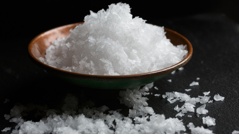 brown bowl of salt flakes with some spilled around it