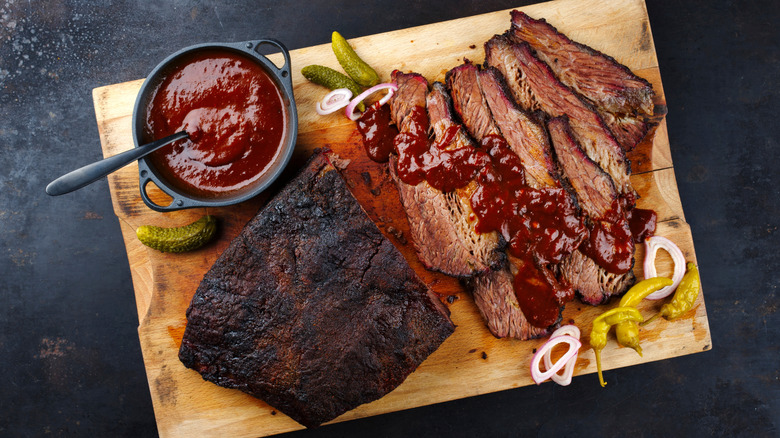 brisket on a wooden board with BBQ sauce, onion and pickles