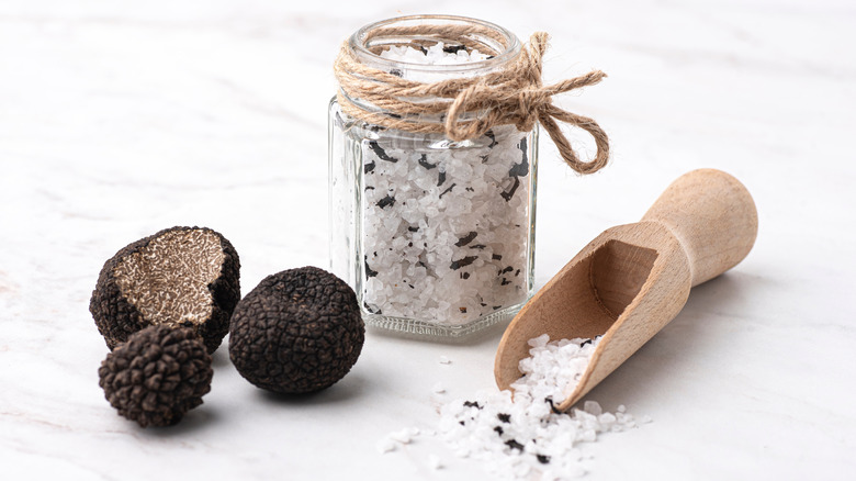 black truffles, a jar of truffle salt and some truffle salt spilling from a wooden shovel
